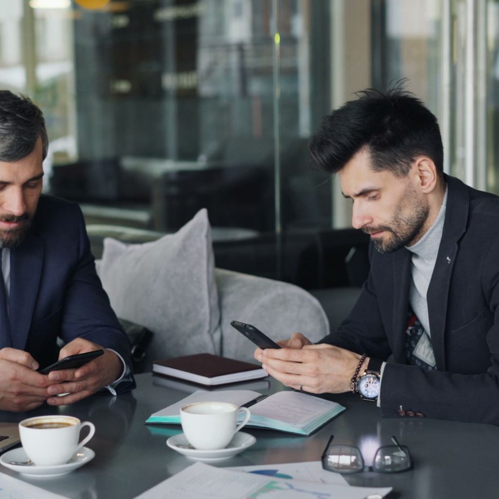 Two businessmen in a cafe working on smartphones and laptops, engaged in a meeting. — Discover Unique Comfort Through Nuro Ma