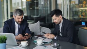Two businessmen in a cafe working on smartphones and laptops, engaged in a meeting. — Discover Unique Comfort Through Nuro Ma