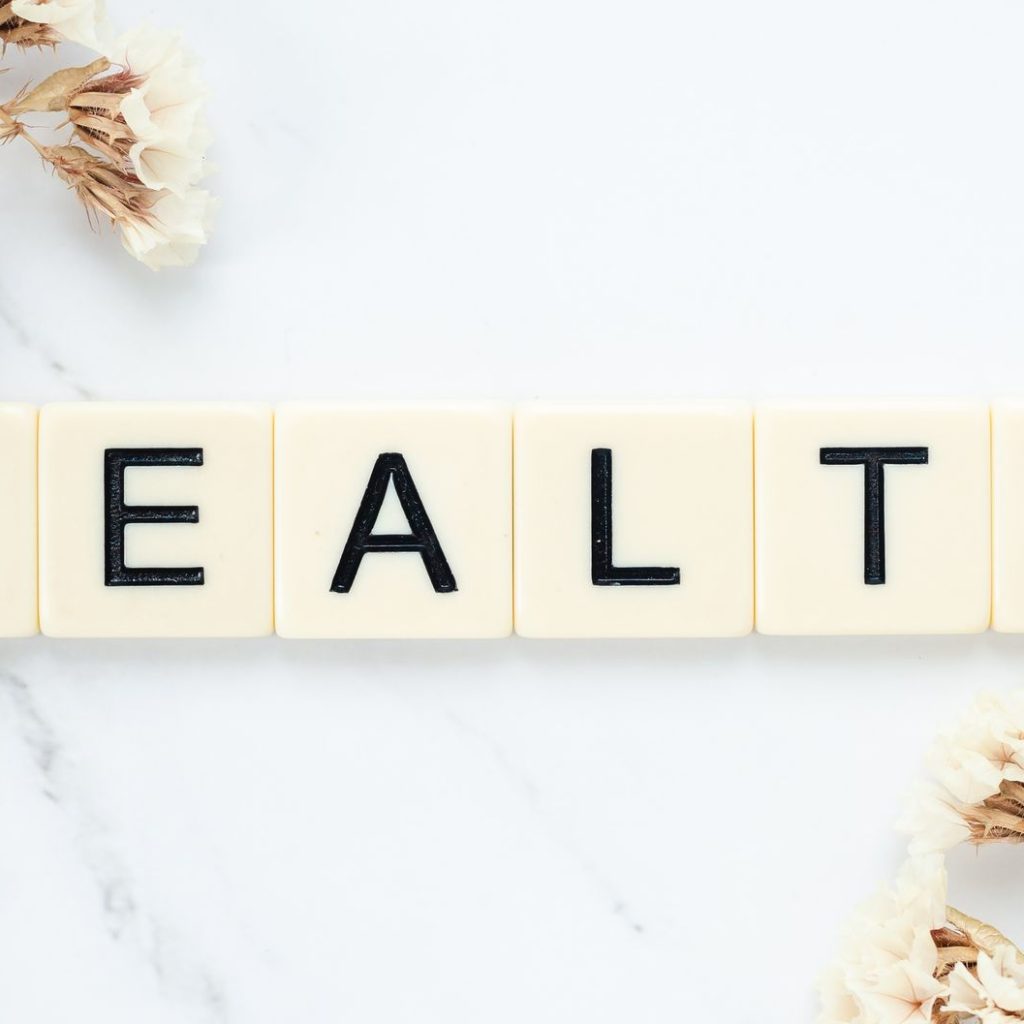 Creative arrangement of scrabble tiles spelling 'Health' with white flowers on a marble surface. — Stuart Piltch Insurance Ex