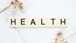 Creative arrangement of scrabble tiles spelling 'Health' with white flowers on a marble surface. — Stuart Piltch Insurance Ex