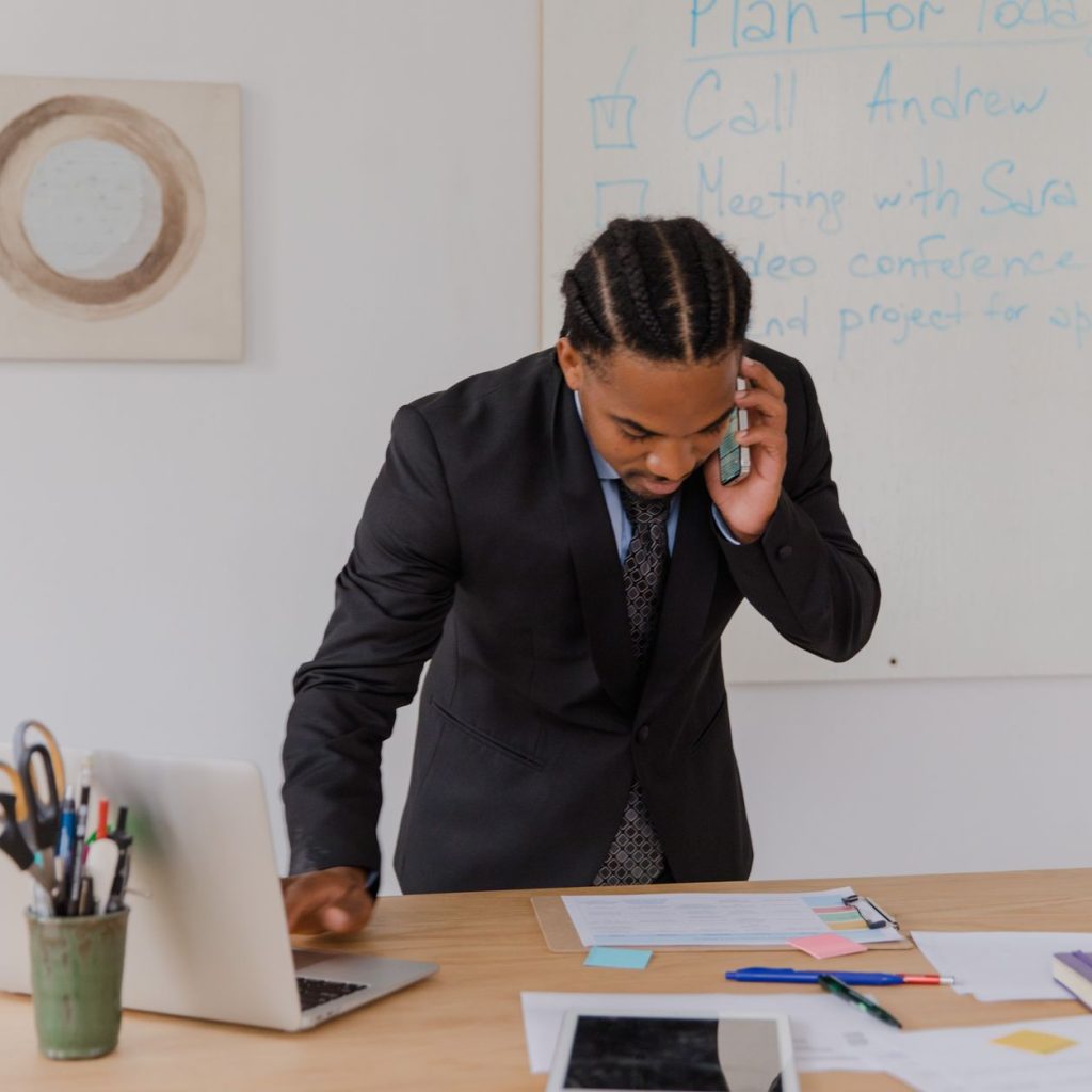 Professional businessman multitasking with phone and laptop at office desk, surrounded by documents. — Top 10 Strains to Look