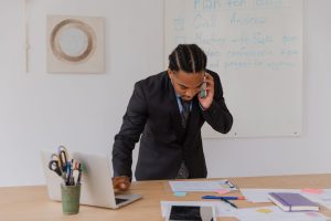 Professional businessman multitasking with phone and laptop at office desk, surrounded by documents. — Top 10 Strains to Look
