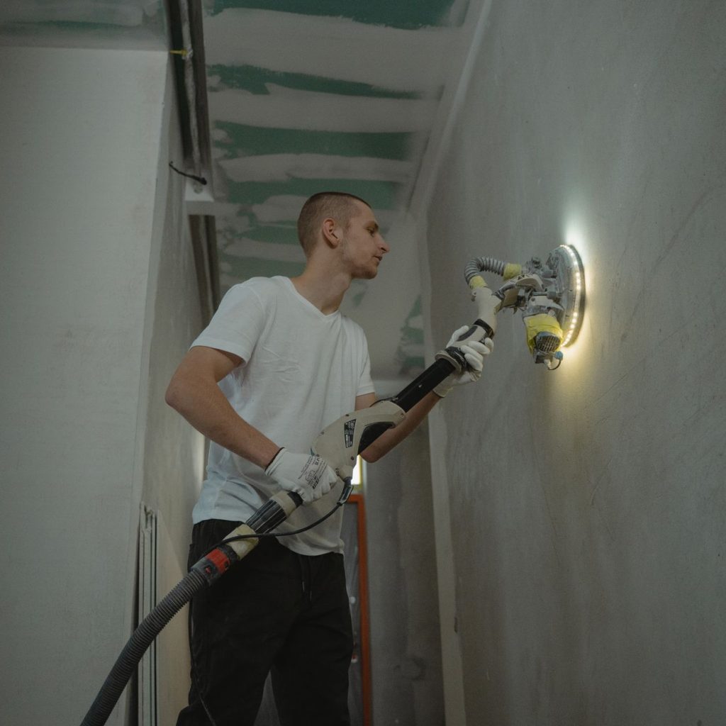 A man sanding an interior wall with an automatic sanding tool during renovation work indoors. — Transforming Spaces with Styl