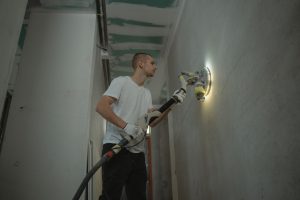 A man sanding an interior wall with an automatic sanding tool during renovation work indoors. — Transforming Spaces with Styl