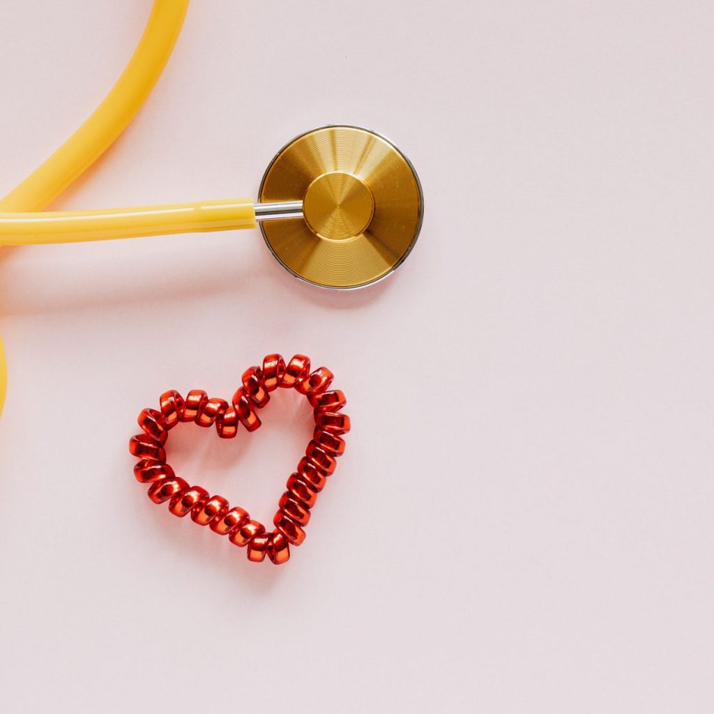 From above of yellow stethoscope near small red bead heart made for San Valentines Day on pale pink surface — Understanding D