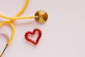 From above of yellow stethoscope near small red bead heart made for San Valentines Day on pale pink surface — Understanding D