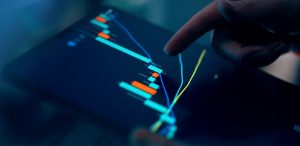 Close-up of a finger pointing at a digital trading chart on a tablet, displaying candlestick patterns and trend lines.